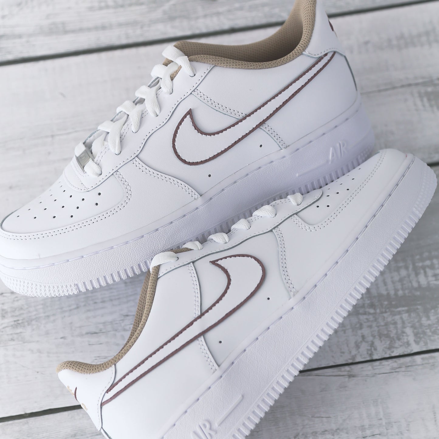 Nike Air Force 1 blanche avec contours marron peints à la main et doublure beige, posée sur fond bois clair