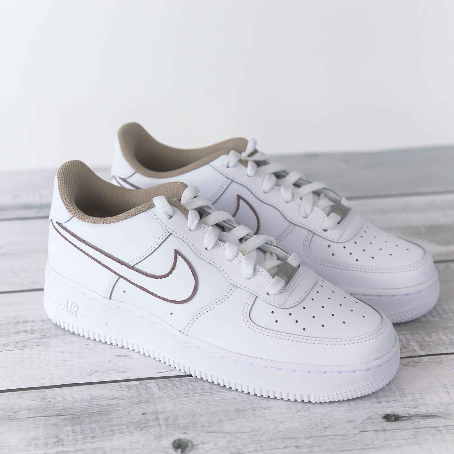 Nike Air Force 1 blanche avec contours marron peints à la main et doublure beige, posée sur fond bois clair