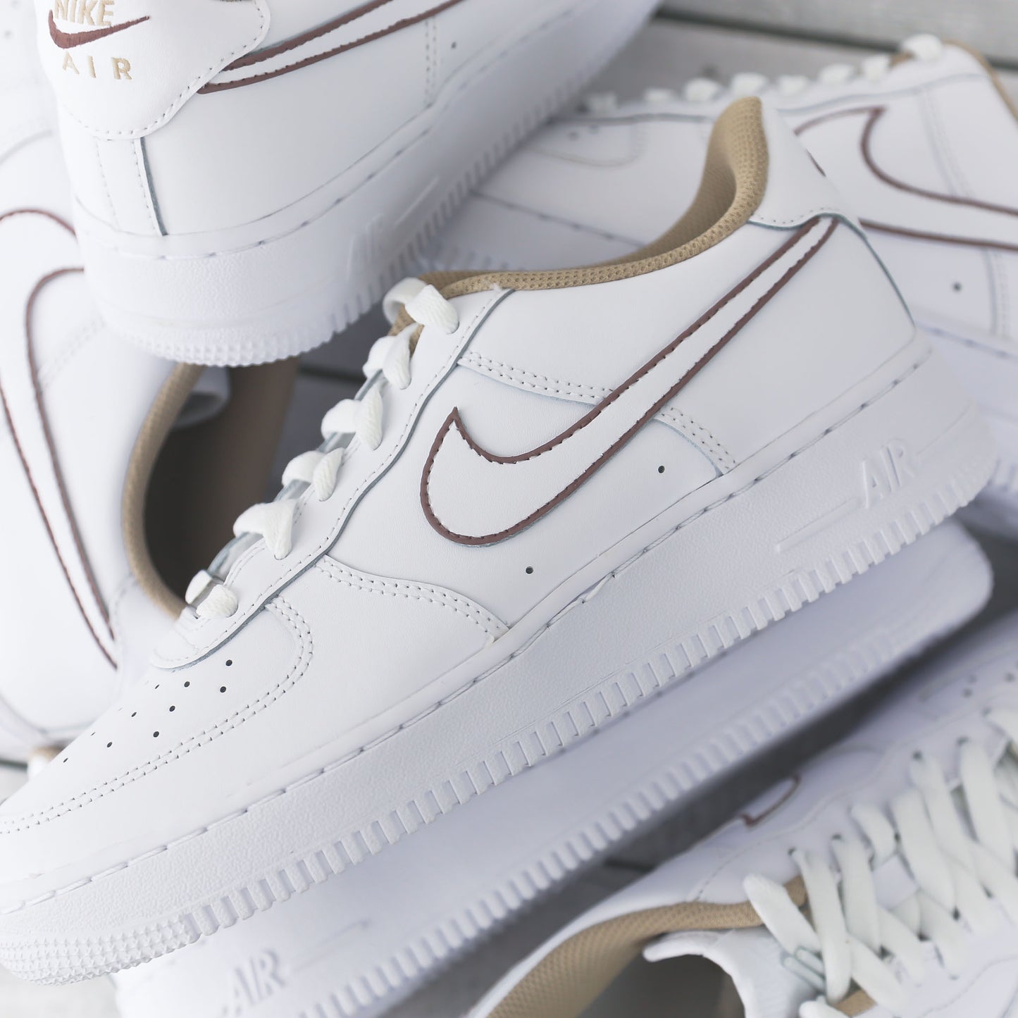Nike Air Force 1 blanche avec contours marron peints à la main et doublure beige, posée sur fond bois clair
