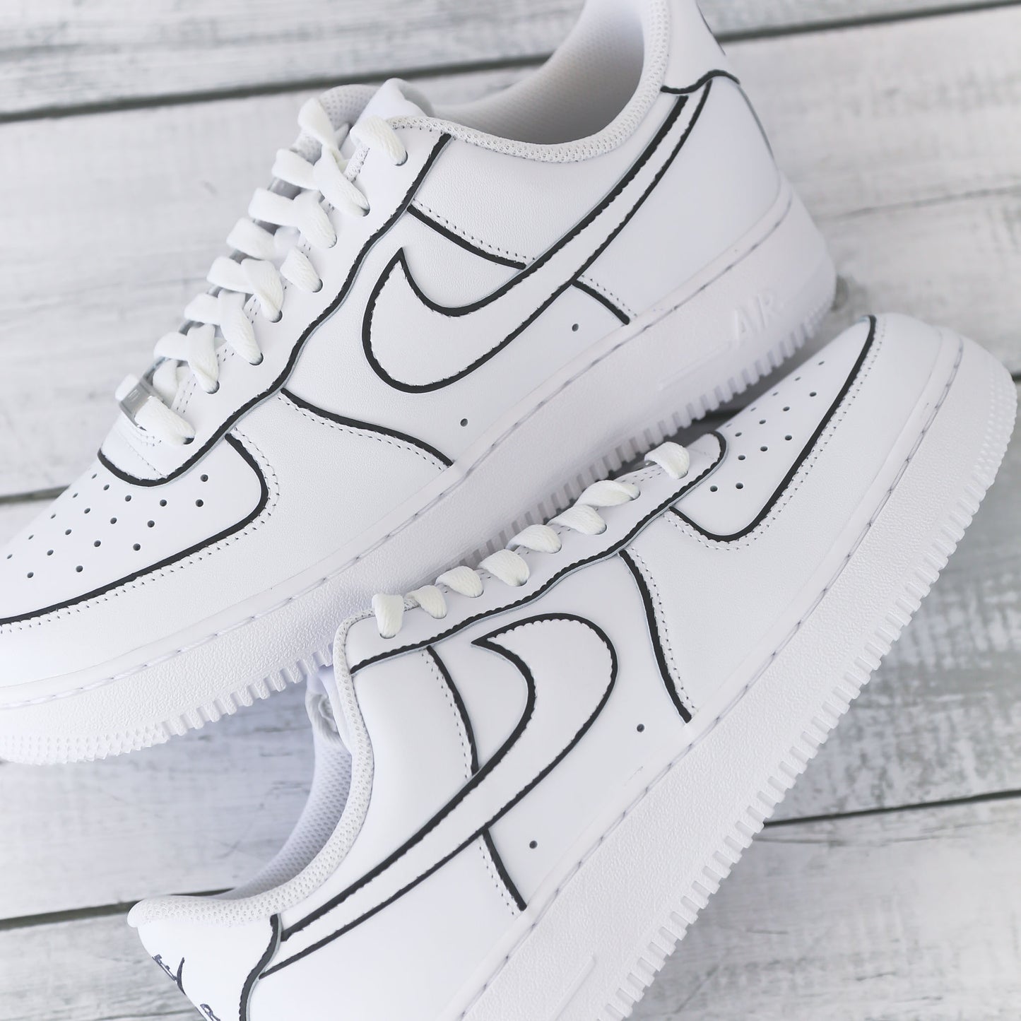 Nike Air Force 1 blanche customisée avec contours noirs brodés, effet dessin, posée sur un fond bois clair