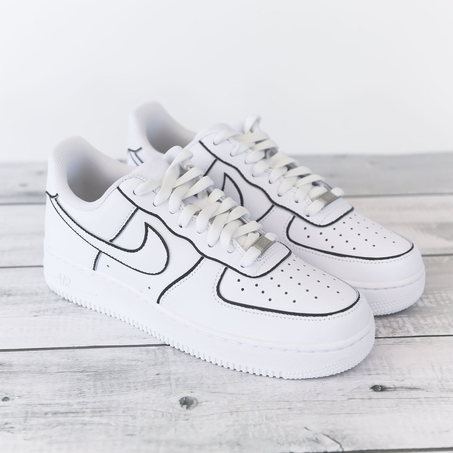 Nike Air Force 1 blanche customisée avec contours noirs brodés, effet dessin, posée sur un fond bois clair