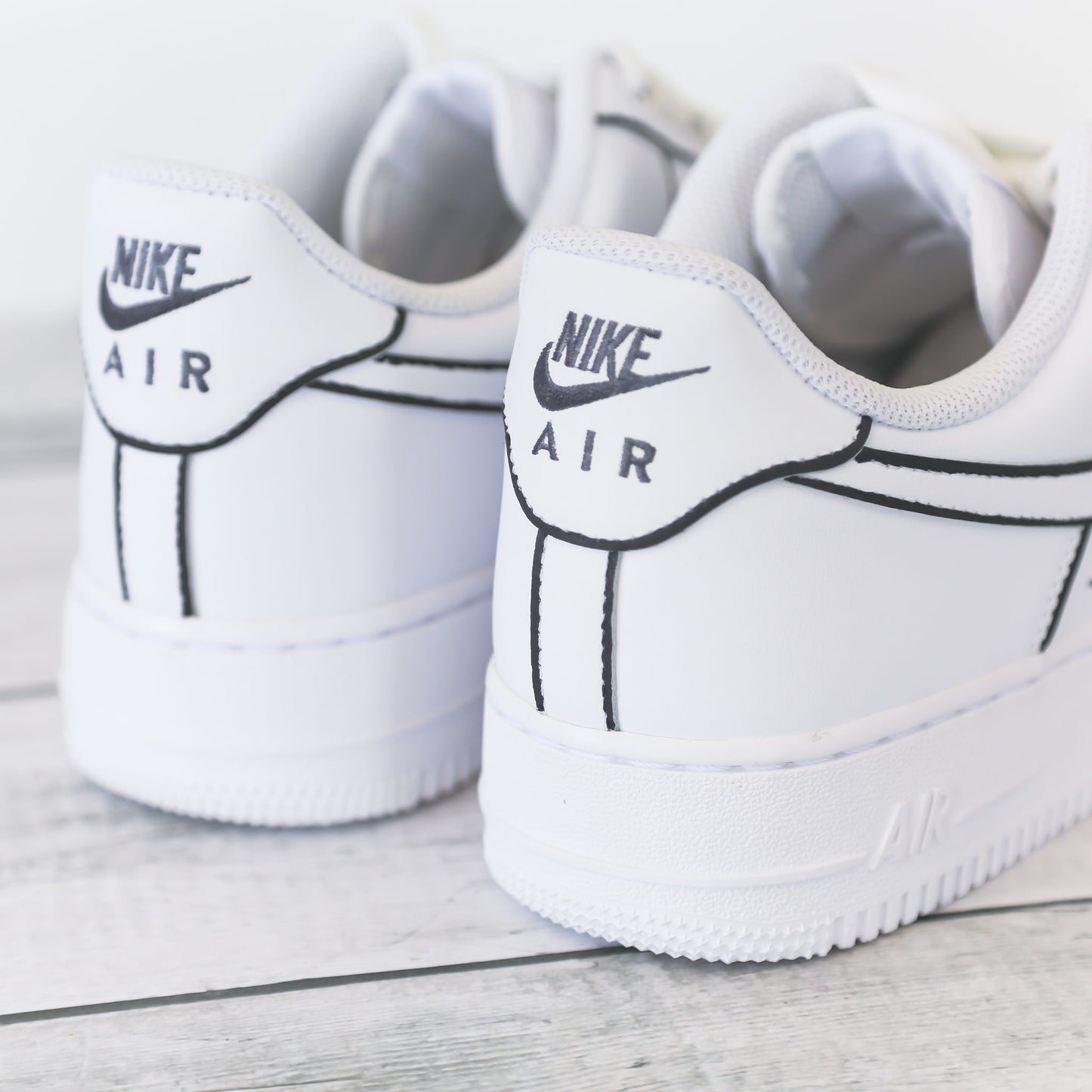 Nike Air Force 1 blanche customisée avec contours noirs brodés, effet dessin, posée sur un fond bois clair