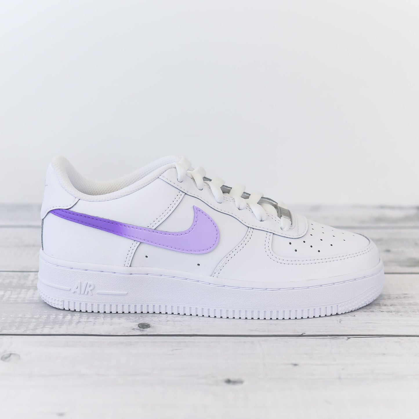 Nike Air Force 1 custom avec swoosh violet pastel sur fond bois clair