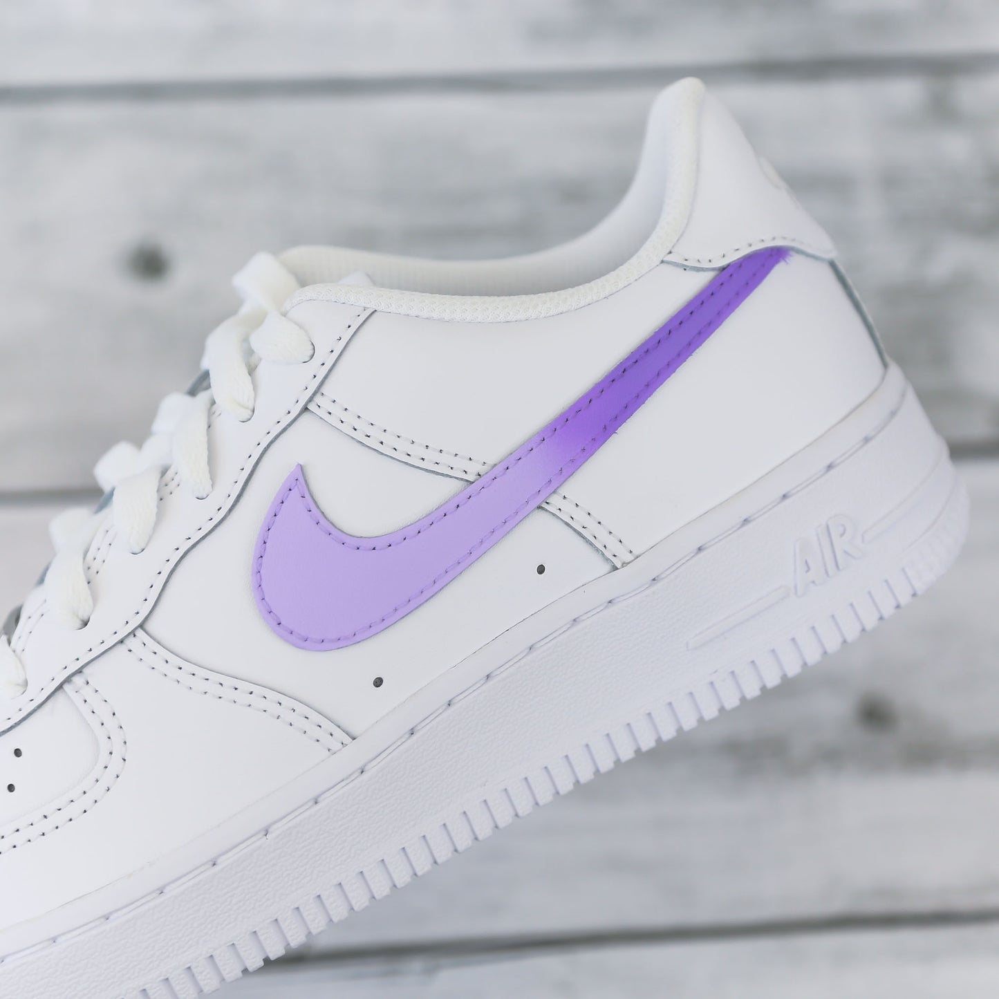 Nike Air Force 1 custom avec swoosh violet pastel sur fond bois clair