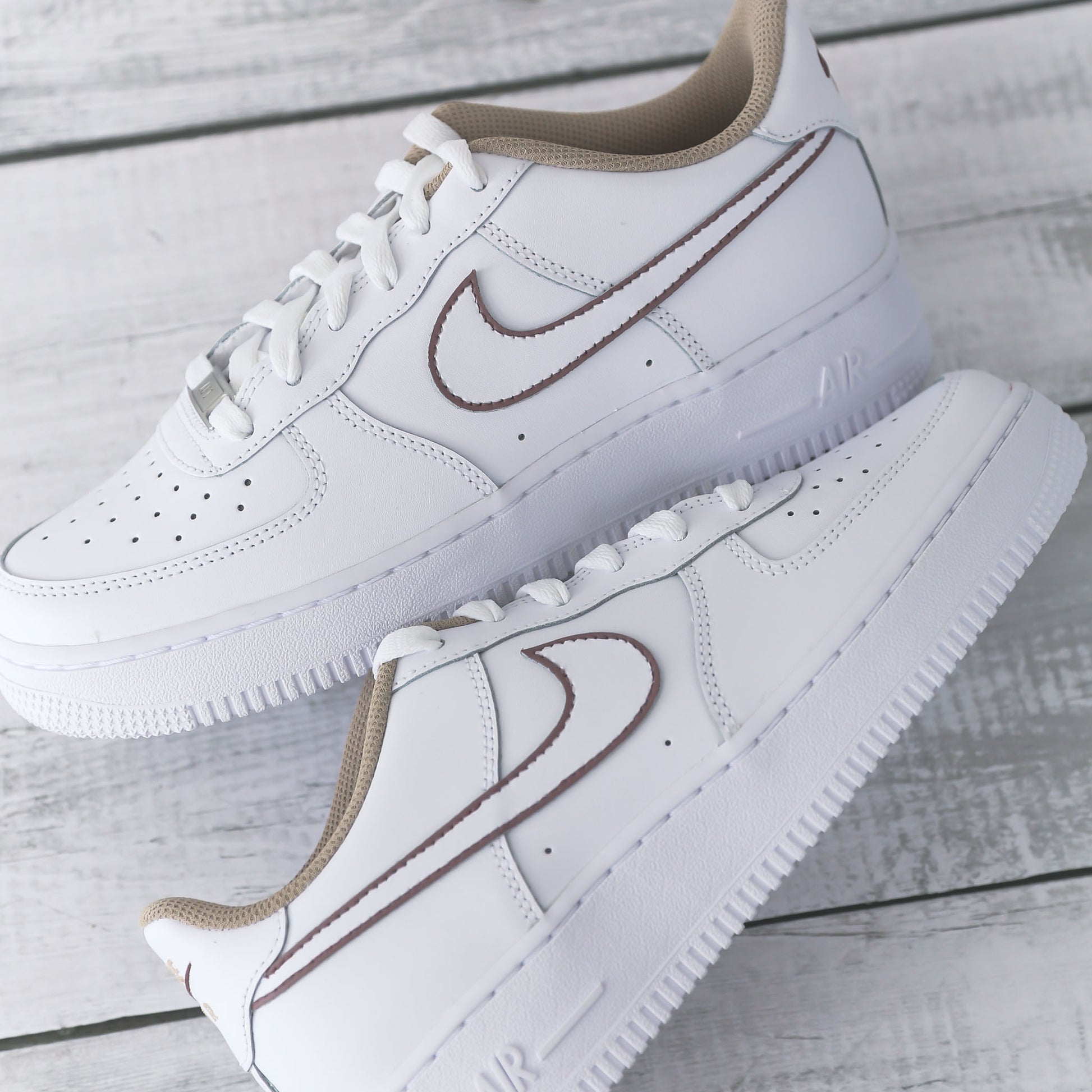 Nike Air Force 1 blanche avec contours marron peints à la main et doublure beige, posée sur fond bois clair