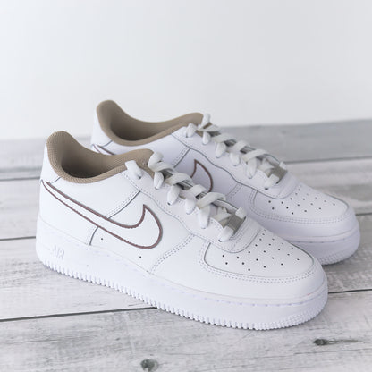 Nike Air Force 1 blanche avec contours marron peints à la main et doublure beige, posée sur fond bois clair