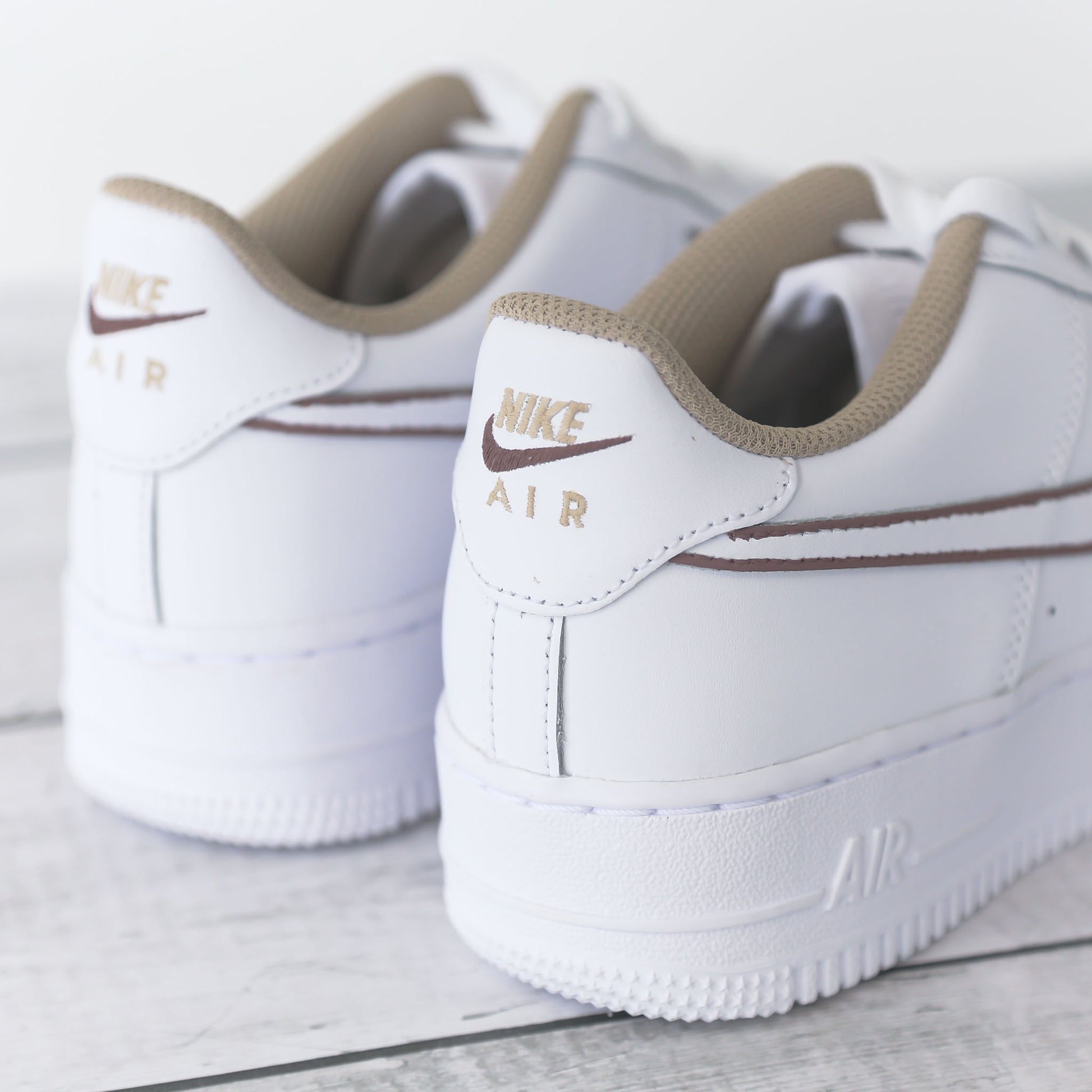 Nike Air Force 1 blanche avec contours marron peints à la main et doublure beige, posée sur fond bois clair