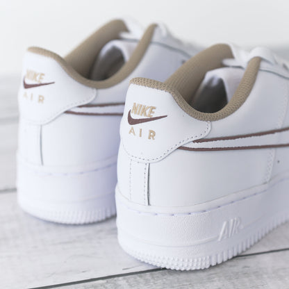 Nike Air Force 1 blanche avec contours marron peints à la main et doublure beige, posée sur fond bois clair