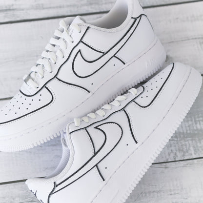 Nike Air Force 1 blanche customisée avec contours noirs brodés, effet dessin, posée sur un fond bois clair