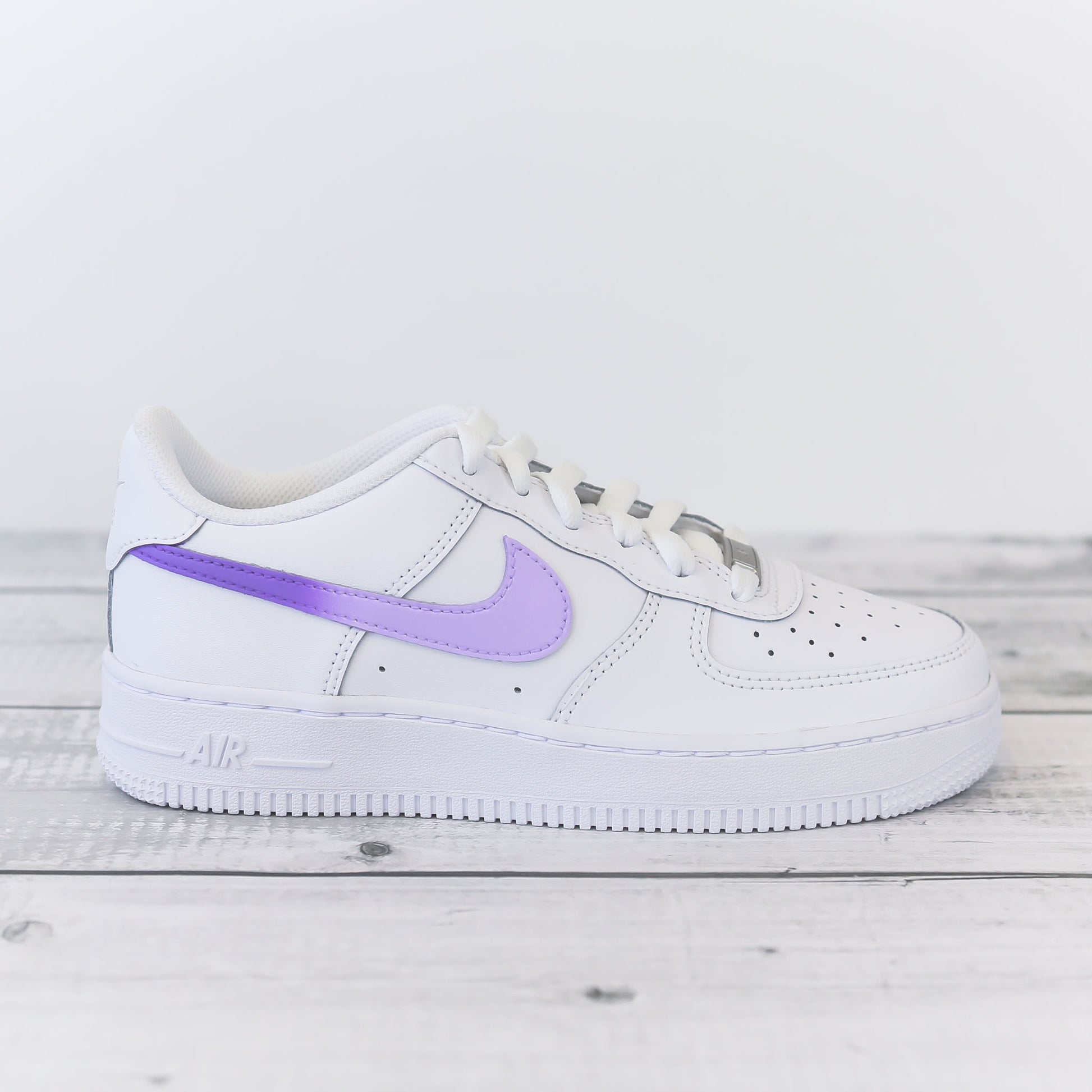 Nike Air Force 1 custom avec swoosh violet pastel sur fond bois clair